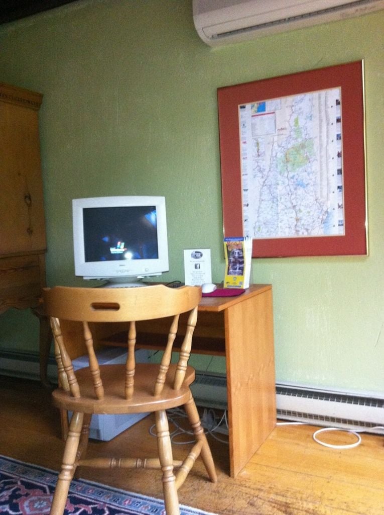 A room with a wooden chair, a desk with a computer monitor, and a framed map on the wall.