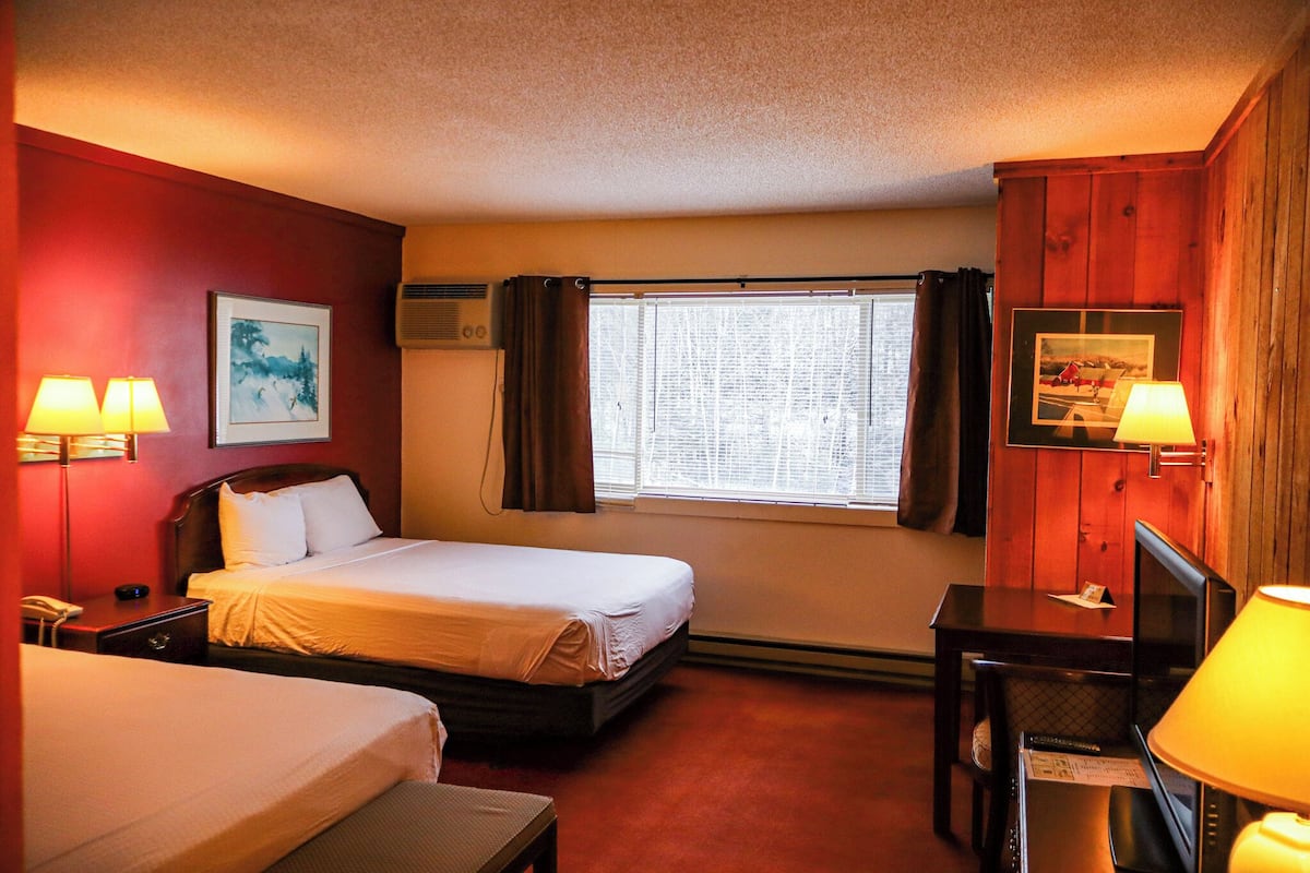 A hotel room with two beds, a desk, a chair, a TV, and a window with curtains.