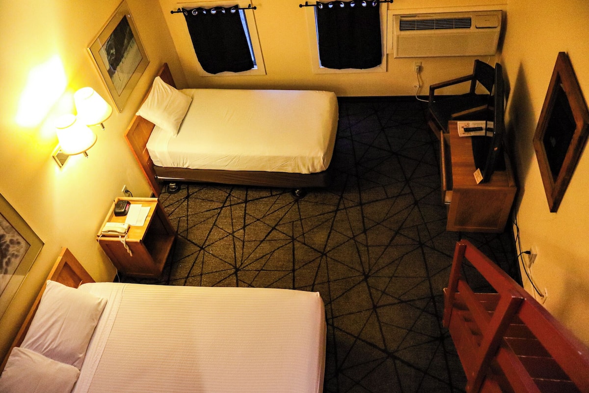 A hotel room with two beds, a desk, a chair, a TV, and a patterned floor.
