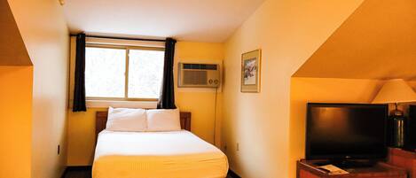 Habitación de hotel con cama, televisor, lámpara, unidad de aire acondicionado y un cuadro en la pared.
