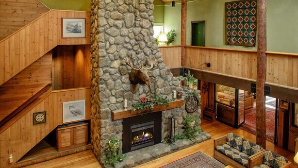 A stone fireplace with a deer head, wooden staircase, and a cozy seating area with a patterned rug. - Snowy Owl Inn And Resort (Waterville Valley)