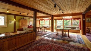 A spacious room with a wooden ceiling, large windows, a dining area, and a seating area with a view of the outdoors. - Snowy Owl Inn And Resort (Waterville Valley)