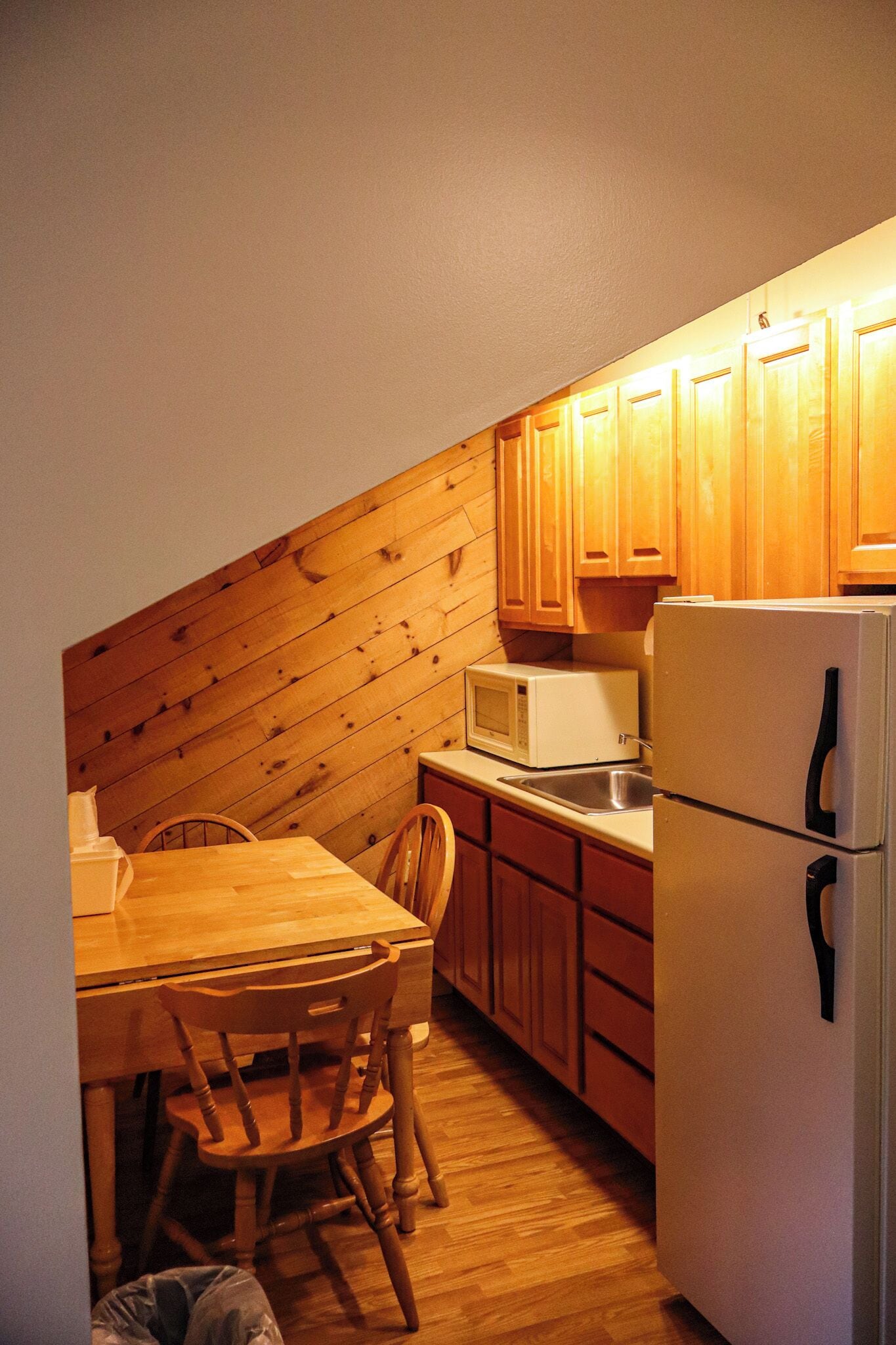 A compact kitchen with wooden cabinets, a microwave, a sink, and a refrigerator.