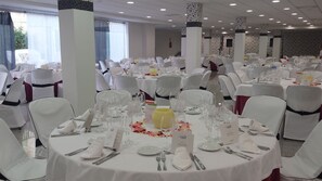 A banquet hall with round tables set for dining, white chairs, and a central column with a yellow vase. - Balneario Palacio de las Salinas (Medina del Campo)