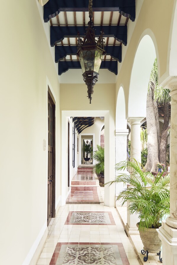 A corridor with a tiled floor, a ceiling with a wooden beam and hanging light fixture, and a view of a staircase leading to an upper level.