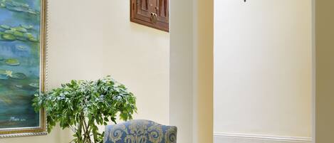 A room with a round table, a chair, a potted plant, a painting, and a view of a pool.