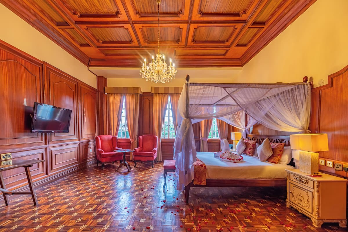 Quarto com uma cama grande, televisão, poltrona vermelha e um lustre.