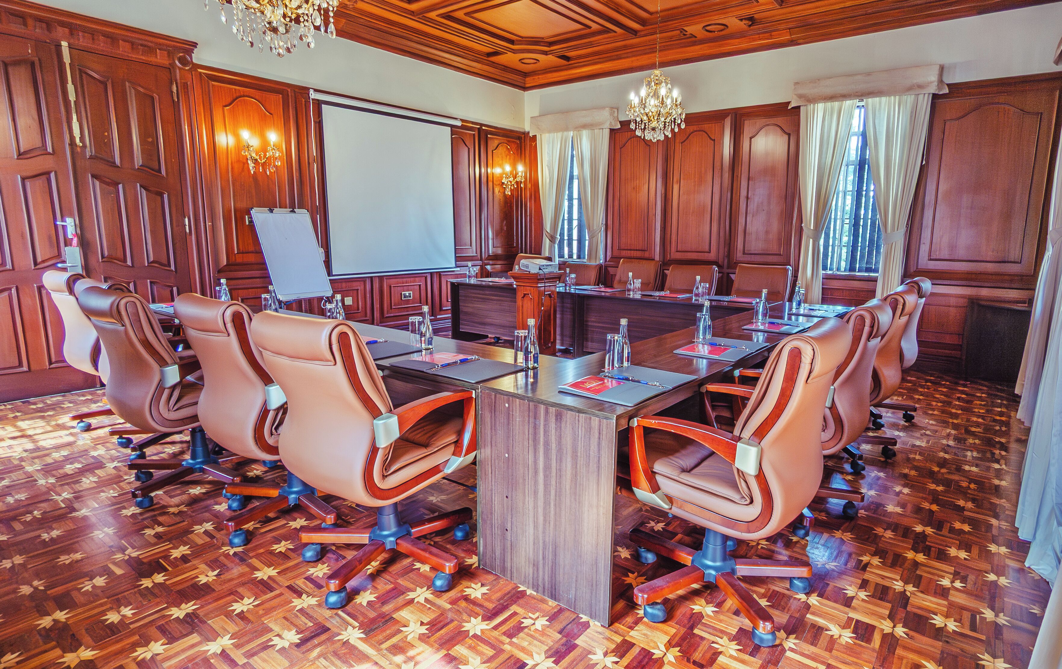 Un salón de conferencias con una gran mesa, sillas de cuero, paneles de madera y candelabros.