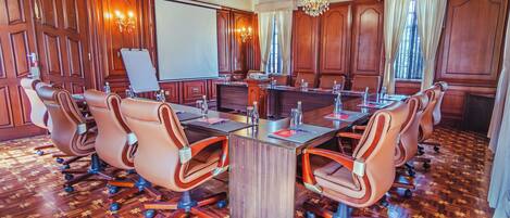 Un salón de conferencias con una gran mesa, sillas de cuero, paneles de madera y candelabros.