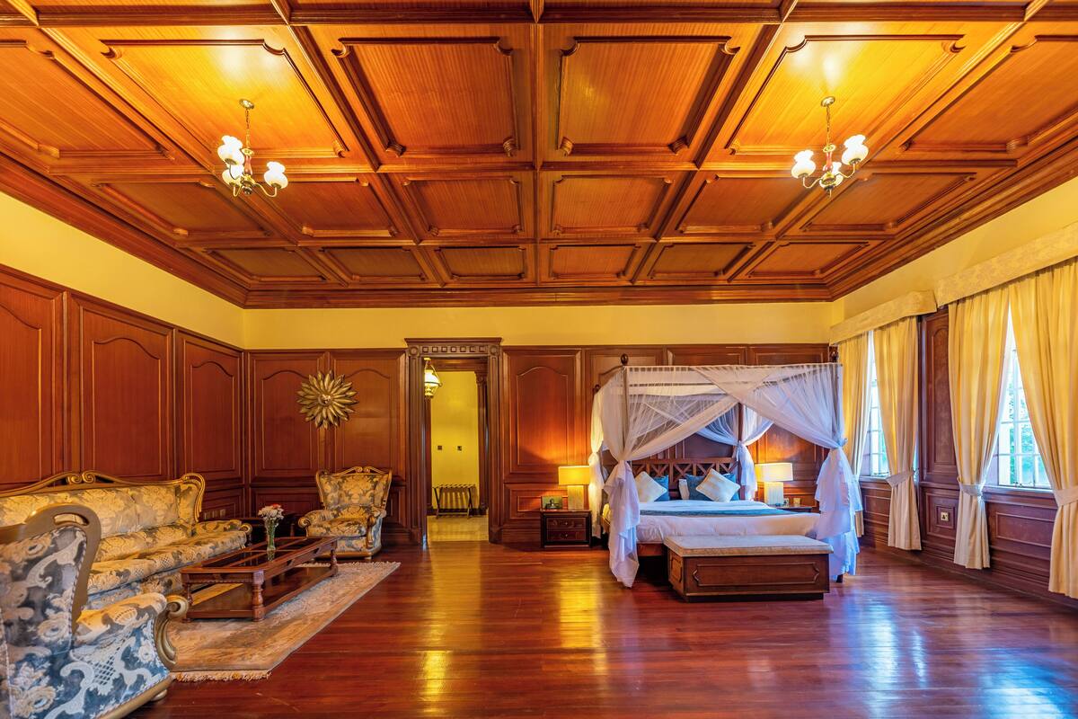 Um quarto espaçoso com uma cama grande, área de estar com sofás e teto de madeira com lustres.