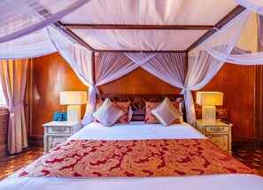 Relax in a spacious room with a four-poster bed and canopy, adorned with a richly patterned bedspread and plush pillows.