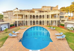 Une grande piscine entourée de chaises longues, un patio couvert et un imposant bâtiment doté de nombreux balcons.