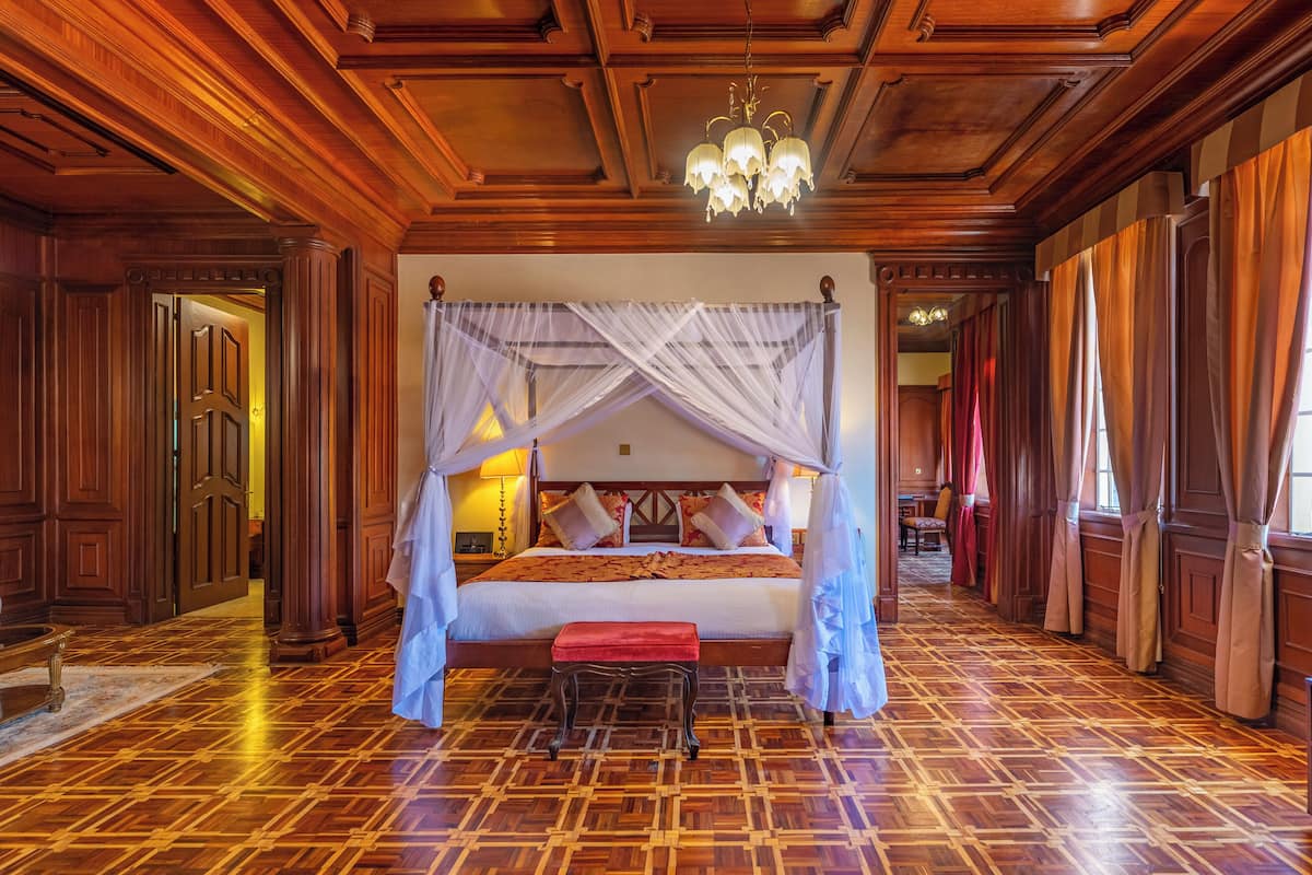 Uma cama king size com dossel, soalho em madeira e um candelabro.