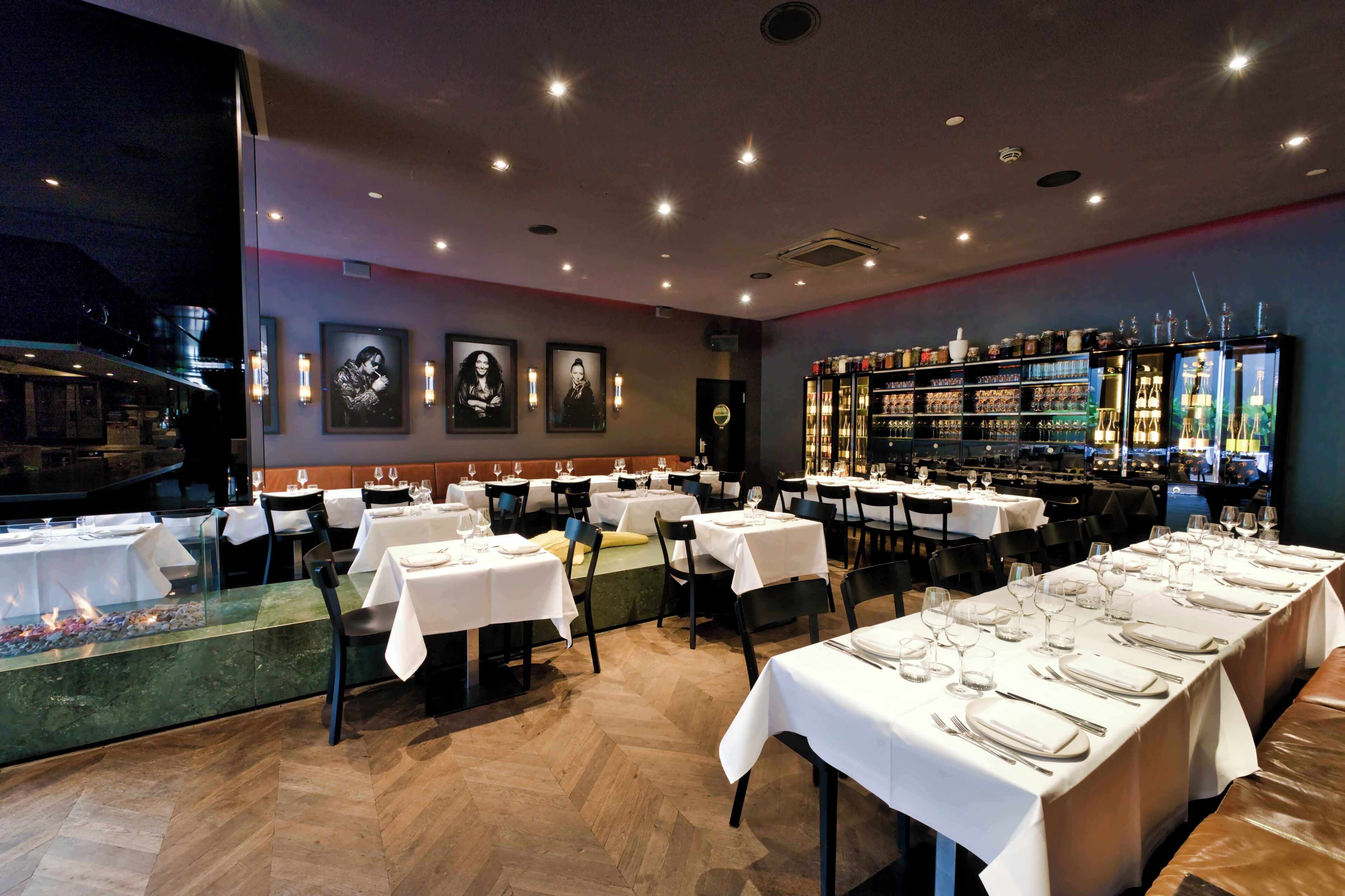 A restaurant with multiple tables set for dining, a bar area with glassware, and a fireplace feature.