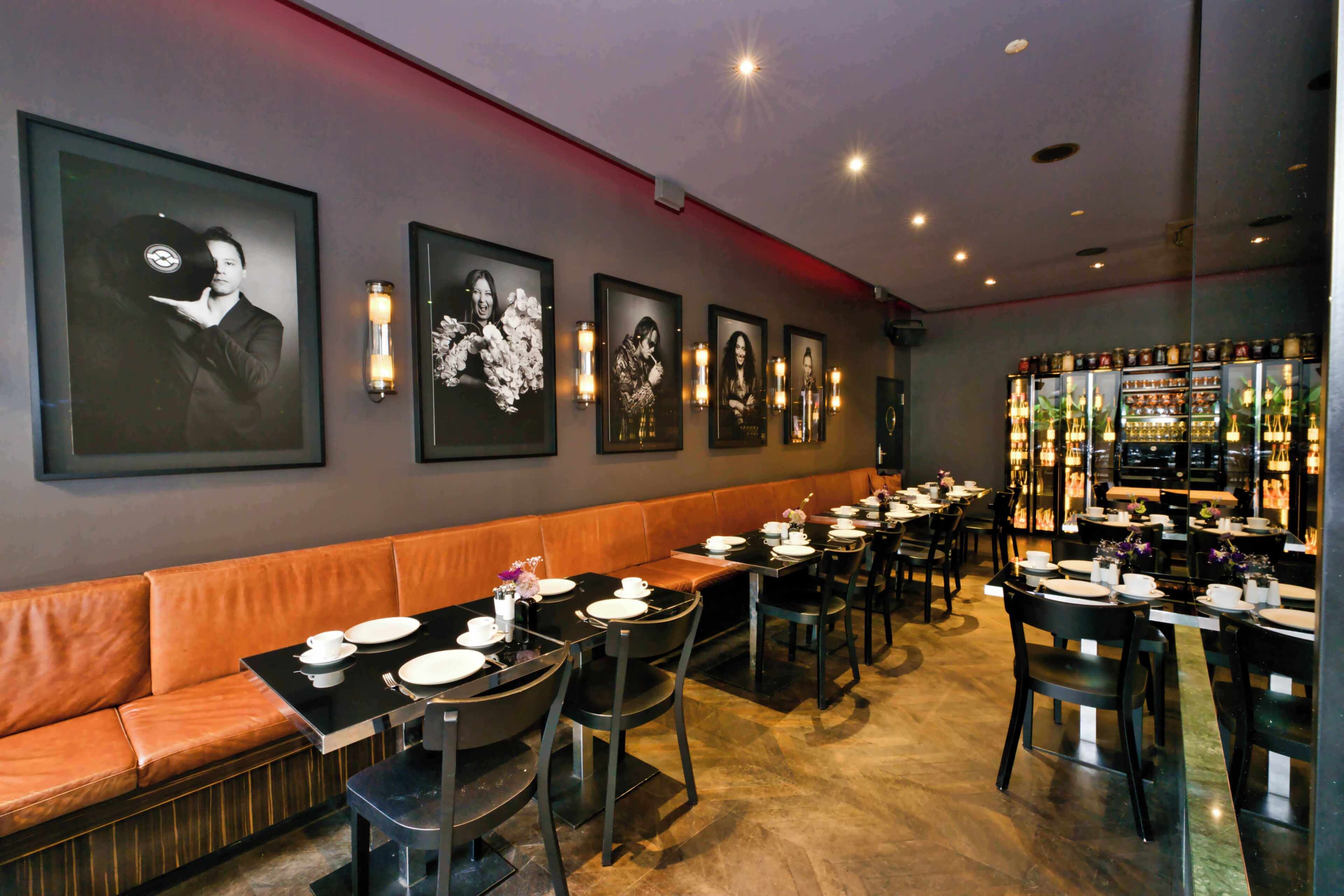 A restaurant with a long counter, cushioned seating, framed pictures on the wall, and a bar area.