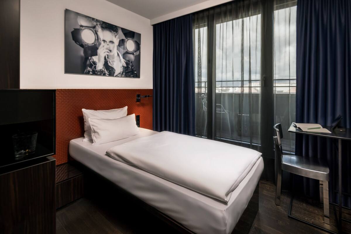 A hotel room with a bed, a TV, a desk, and a window with curtains.