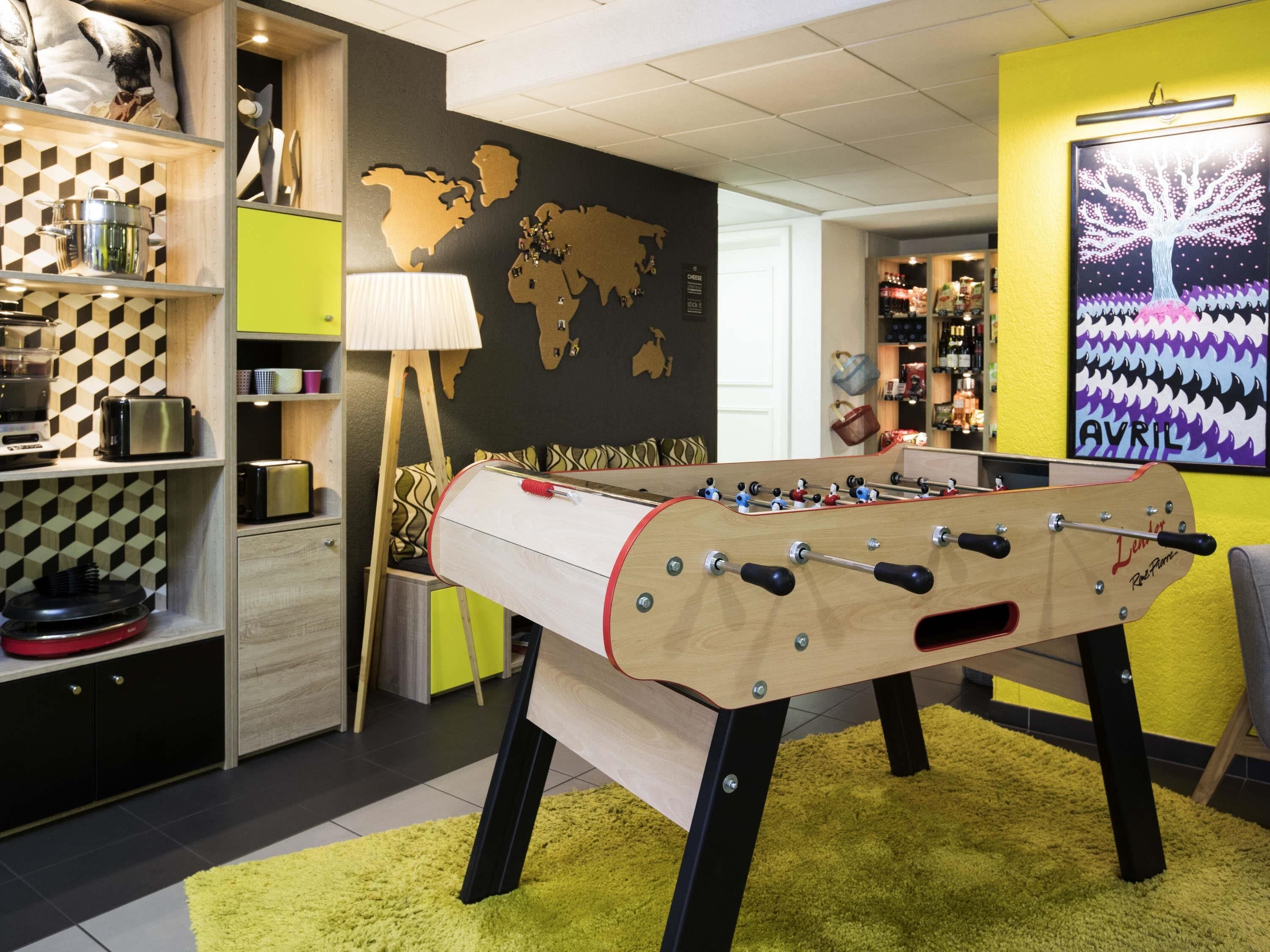 Een kamer met een tafelvoetbaltafel, een wereldkaart aan de muur en een plank met keukenapparatuur.