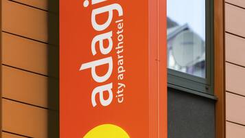 A vertical sign with the text "access adagio city apartment hotel" and a yellow circle logo.