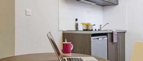 A laptop on a round table with a pink mug, a bottle, and a bowl of pasta.