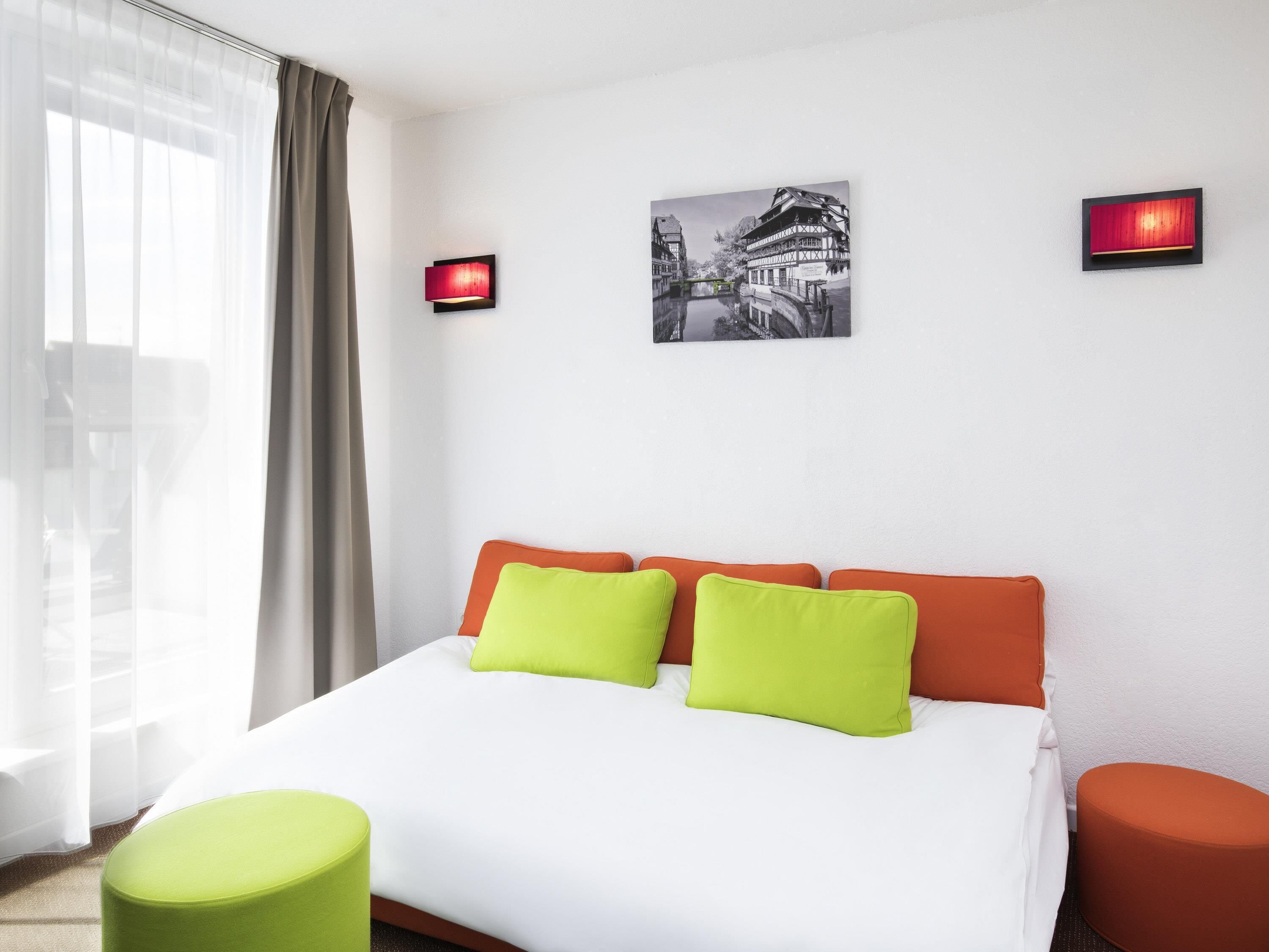 Ein Hotelzimmer mit einem Bett, zwei Kissen, einem Nachttisch, einer Lampe und einem Bild an der Wand.