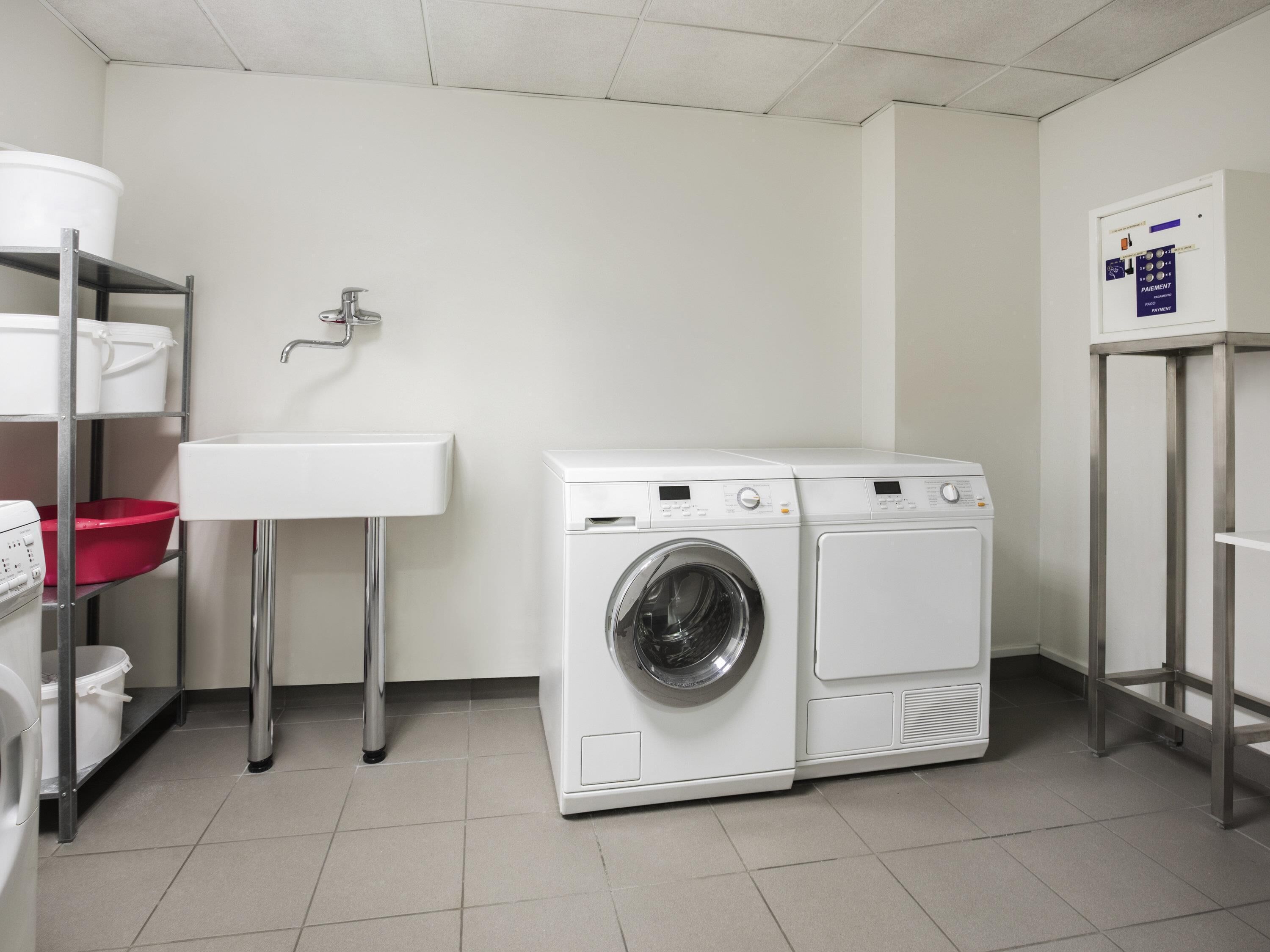 Un cuarto de lavandería con lavadora, pileta y estantes con cestos de ropa.