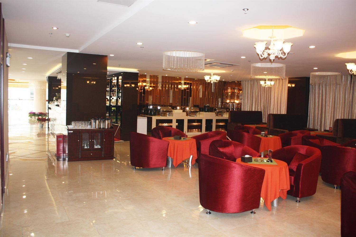 A spacious lobby with a bar area, red upholstered chairs, and a polished marble floor.