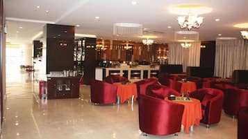 A spacious lobby with a bar area, red upholstered chairs, and a polished marble floor.