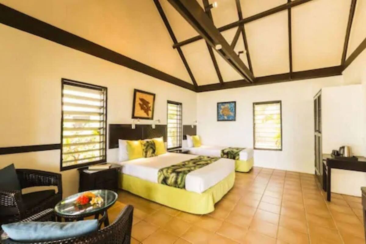 A hotel room with a bed, two bedside tables, a chair, a small table with a glass top, and a window with blinds.