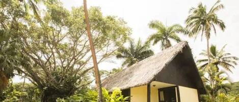 A thatched-roof bungalow with an open porch, surrounded by lush tropical vegetation.