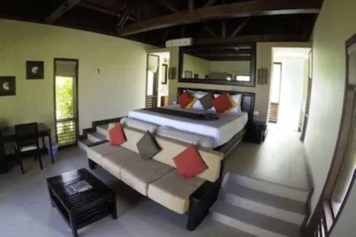 A bedroom with a bed, a sofa, a coffee table, and a mirror.