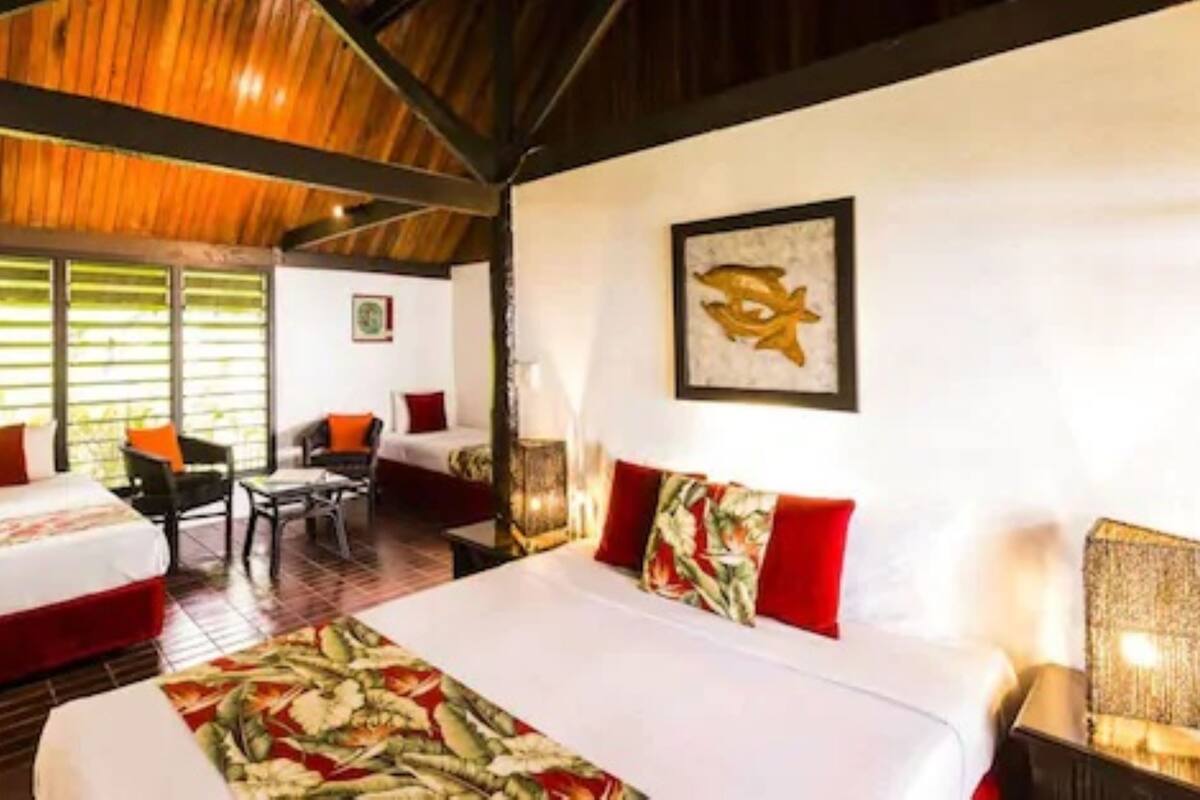 A hotel room with a large bed, two smaller beds, a desk, and a chair.