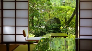 A traditional Japanese room with tatami flooring, a low table, and a view of a lush garden through shoji screens.