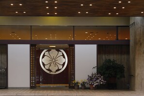 A modern building entrance with a large decorative door, potted plants, and a wooden ceiling.
