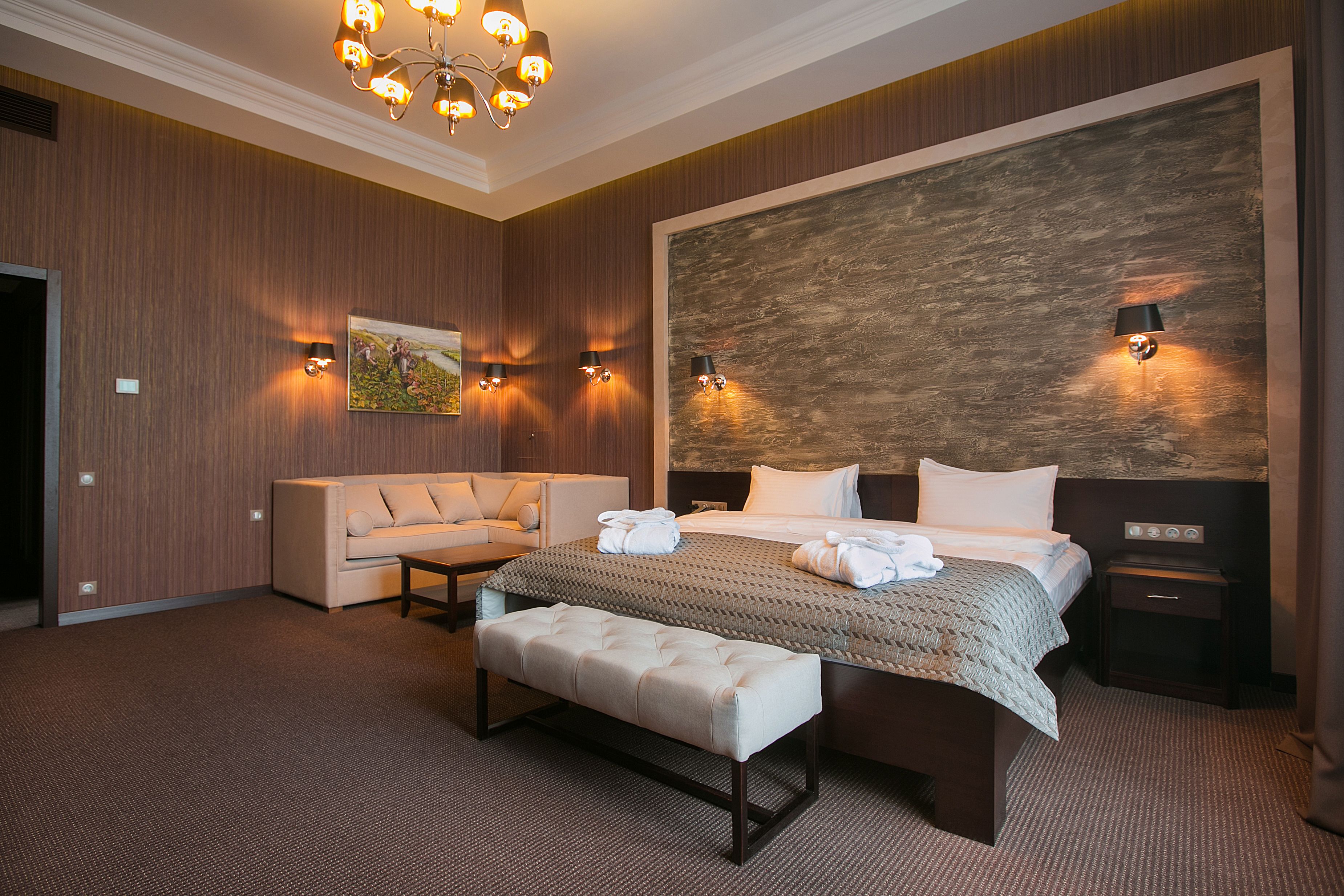 A hotel room with a large bed, a sofa, a bench, and a wall-mounted artwork.