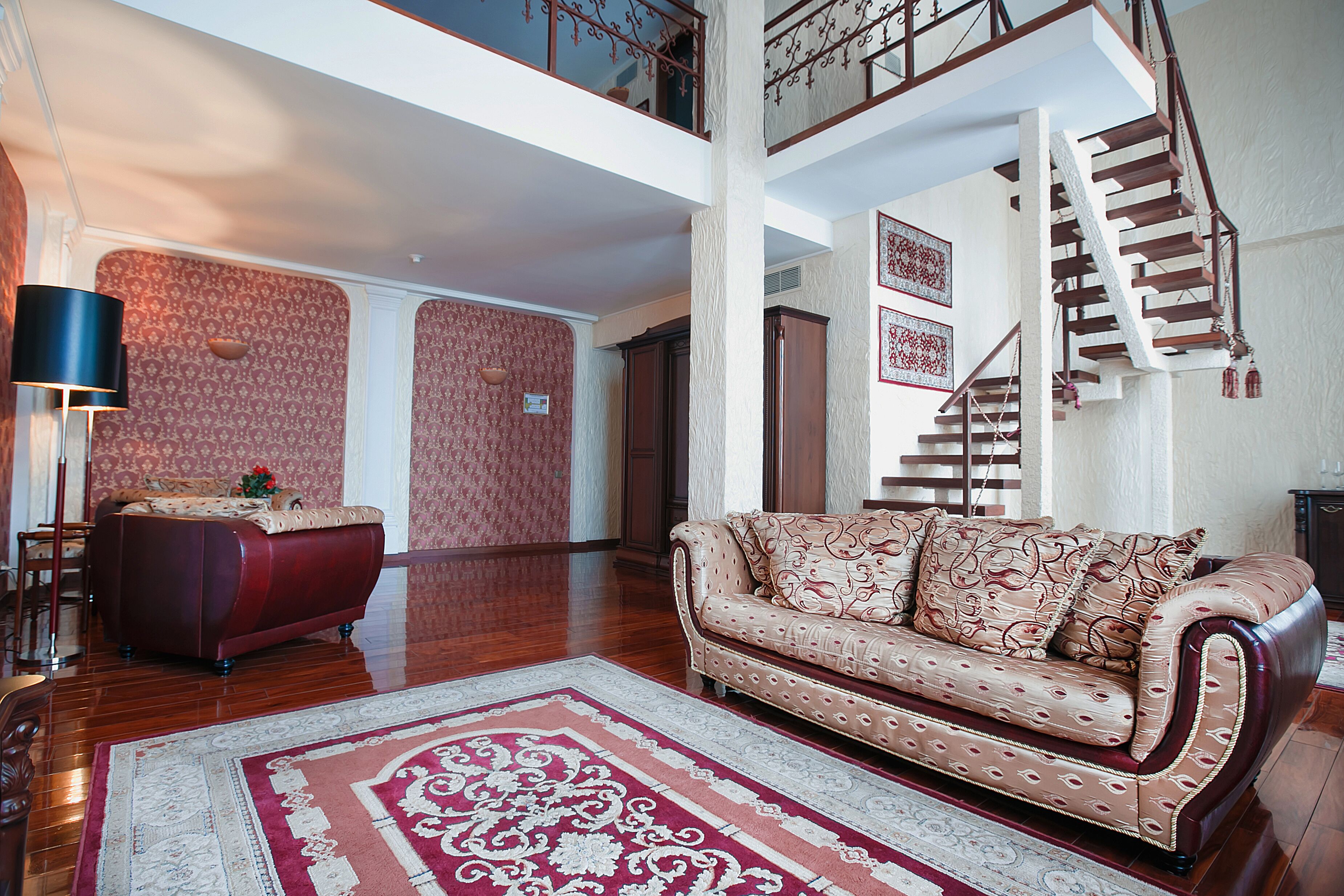 Un salón espacioso con un sofá rojo, un tapete estampado y una escalera que sube a un nivel superior.