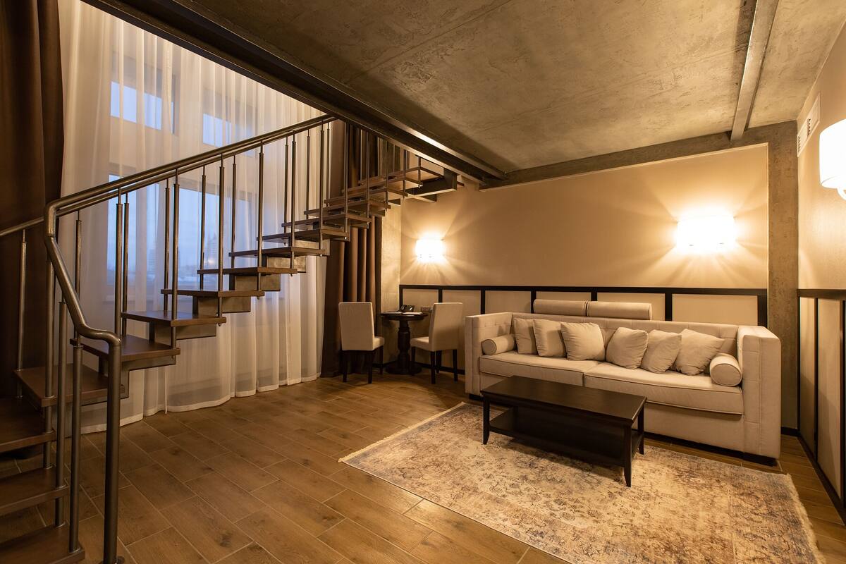 A modern living room with a staircase, a sofa, a coffee table, and a rug.