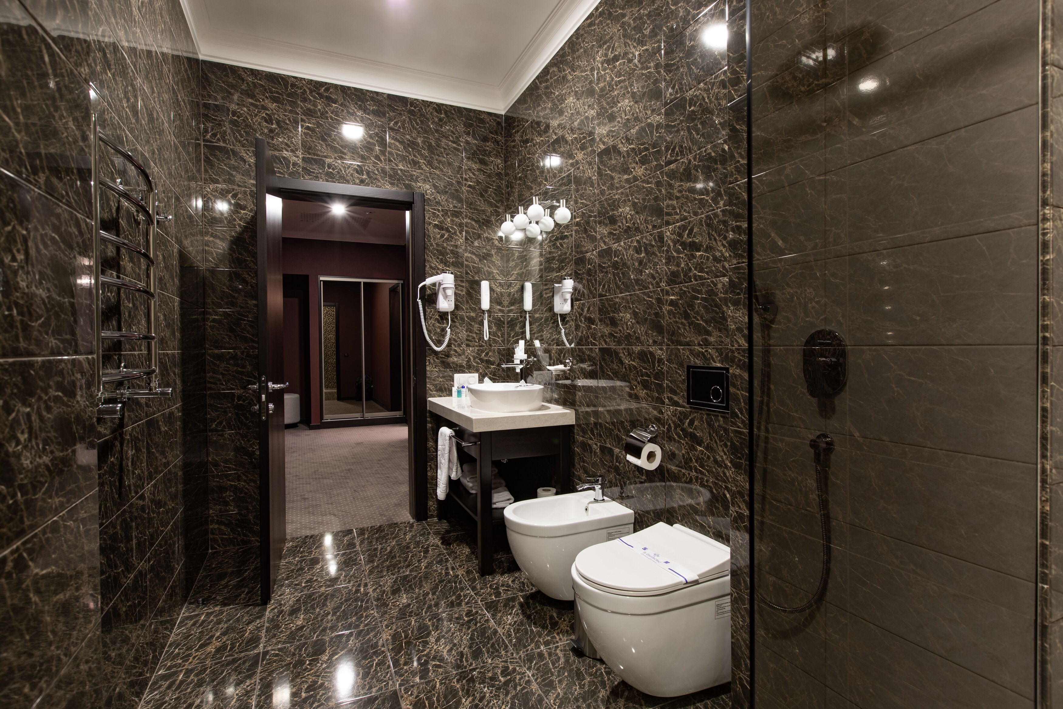 A modern bathroom with a marble floor, a sink, two toilets, a shower, and a vanity with a mirror and lights.