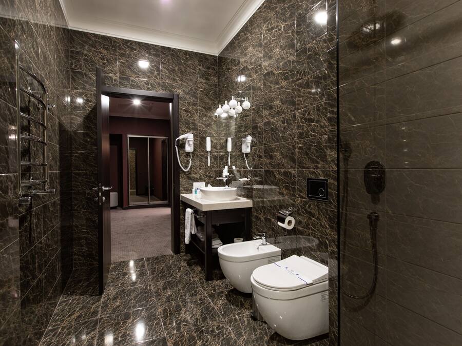 A modern bathroom with a marble floor, a sink, two toilets, a shower, and a vanity with a mirror and lights.