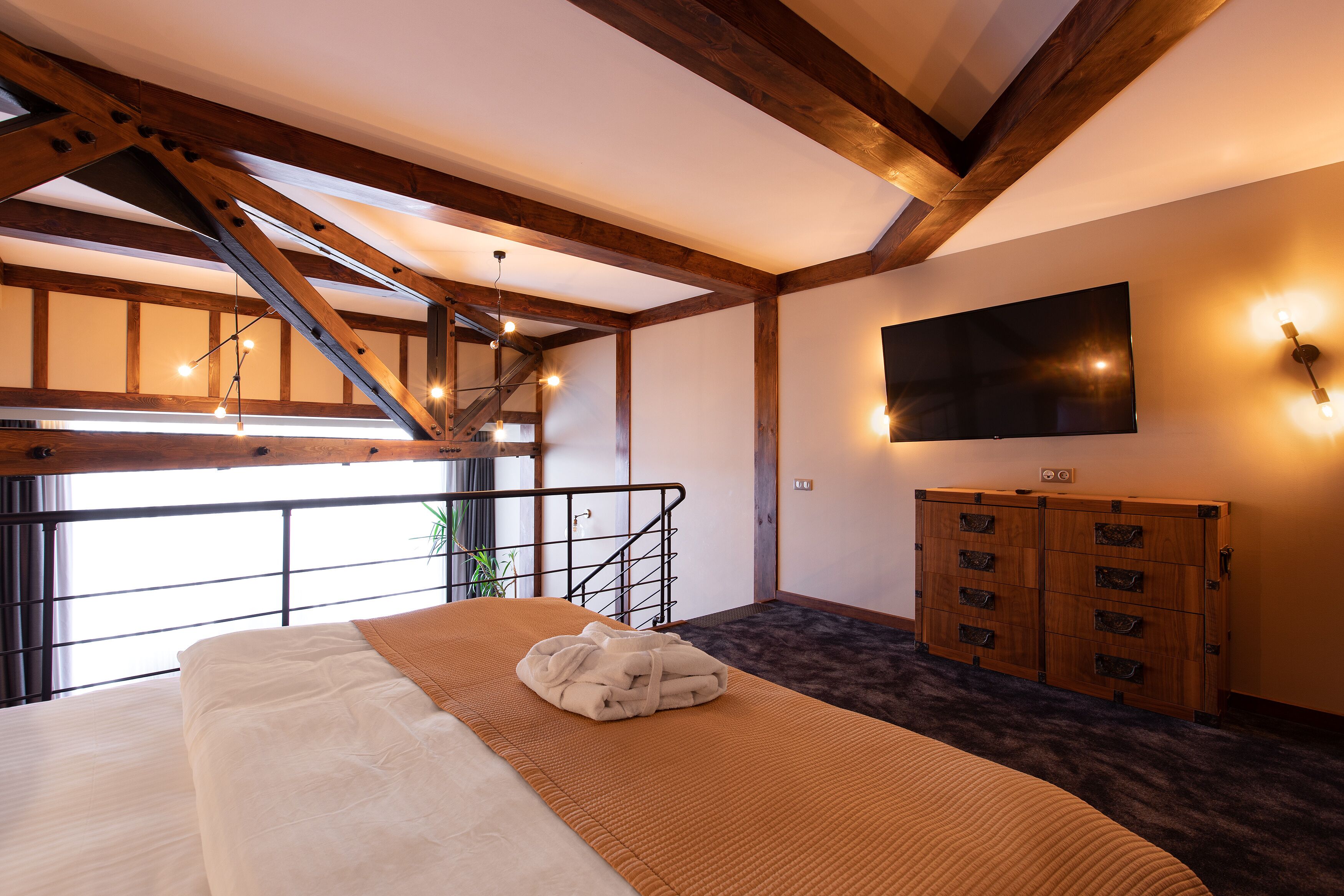 A hotel room with a large bed, wooden beams, a TV, and a staircase.