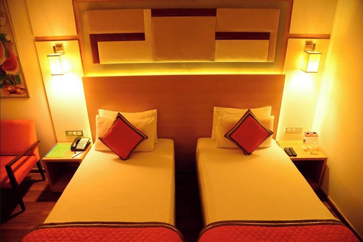 A hotel room with two beds, each with a pillow and a bedside table.