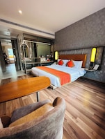 A modern hotel room with a large bed, a wooden table, and a seating area.