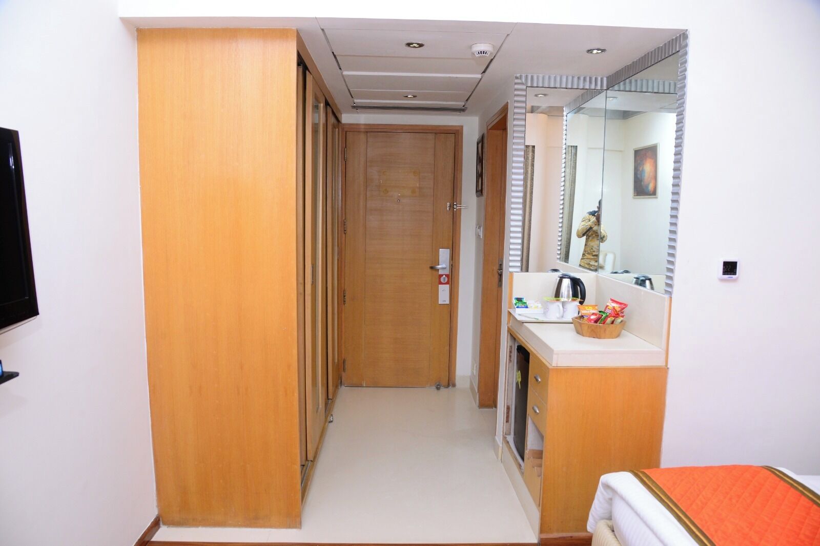 Camera d'albergo con un armadio in legno, uno specchio, un lavandino con articoli da toilette e un letto con coperta arancione.