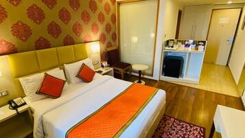Habitación de hotel con una cama grande, una mesita de noche con lámpara, un escritorio pequeño con silla y un minibar.