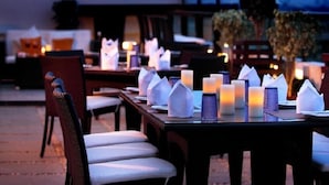 Uma área de refeições ao ar livre com mesas preparadas para dois, cada uma com guardanapos brancos e velas.