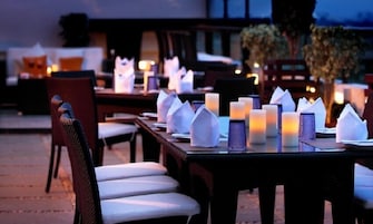An outdoor dining area with tables set for two, each with white napkins and candles.