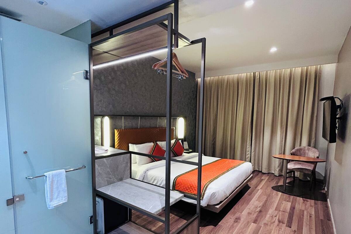 A modern hotel room with a glass partitioned bed, a wooden floor, a small table, and a chair.