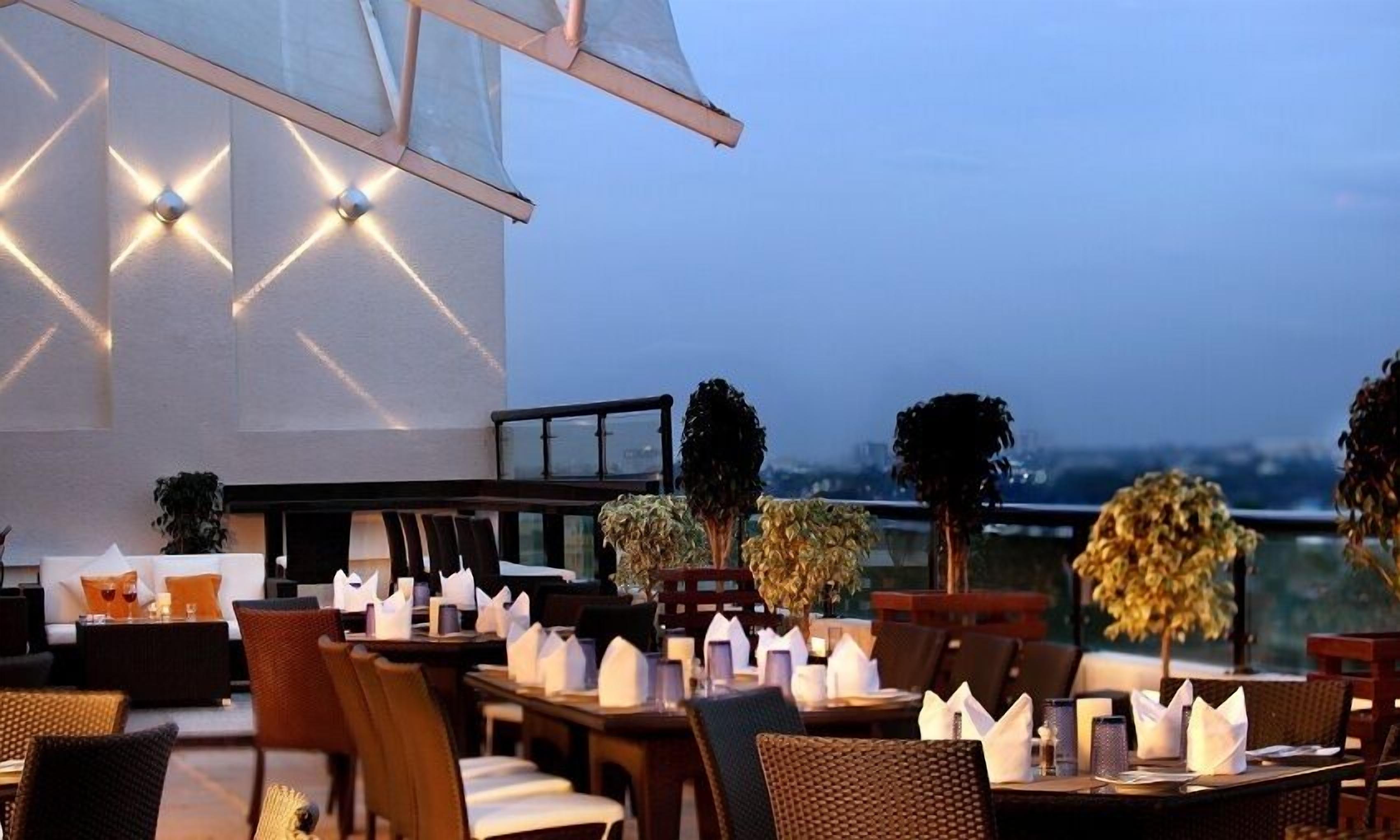 An outdoor dining area with tables and chairs, a railing, and a view of the cityscape.