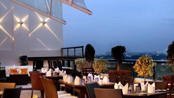An outdoor dining area with tables and chairs, a railing, and a view of the cityscape.