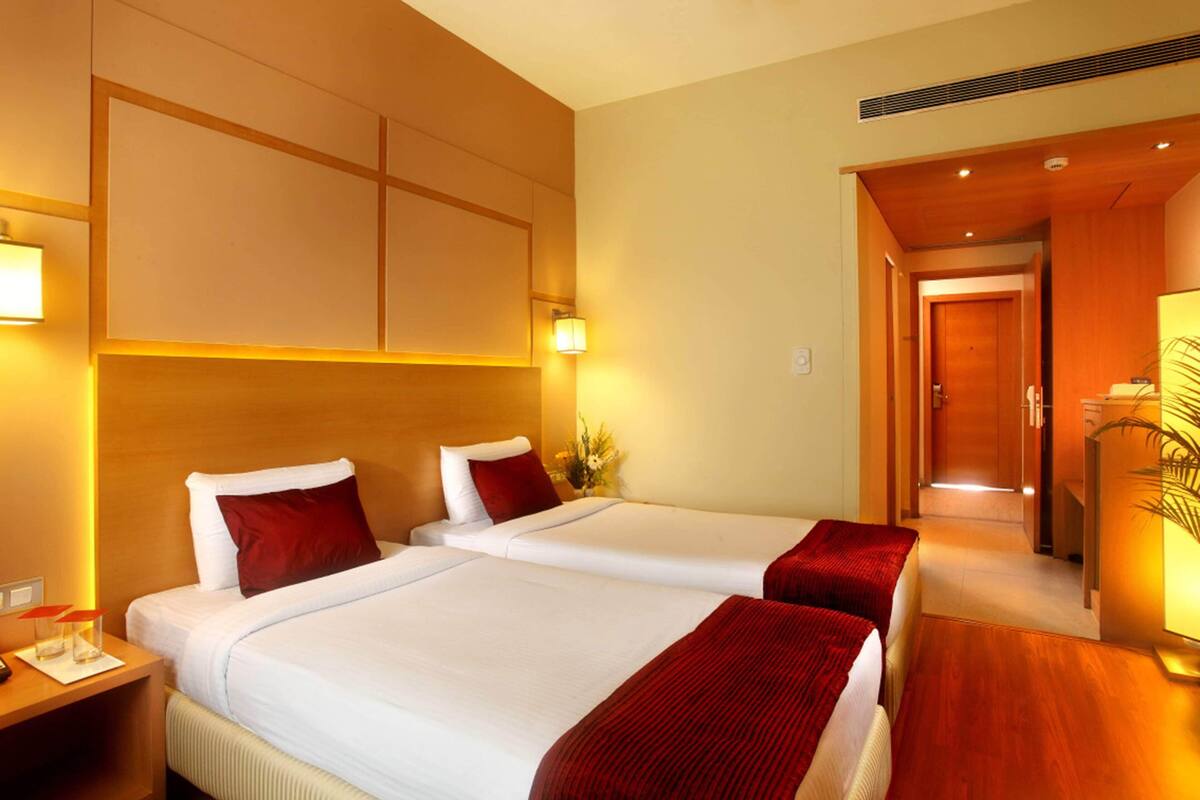 A hotel room with two beds, a wooden headboard, bedside lamps, and a wooden desk.