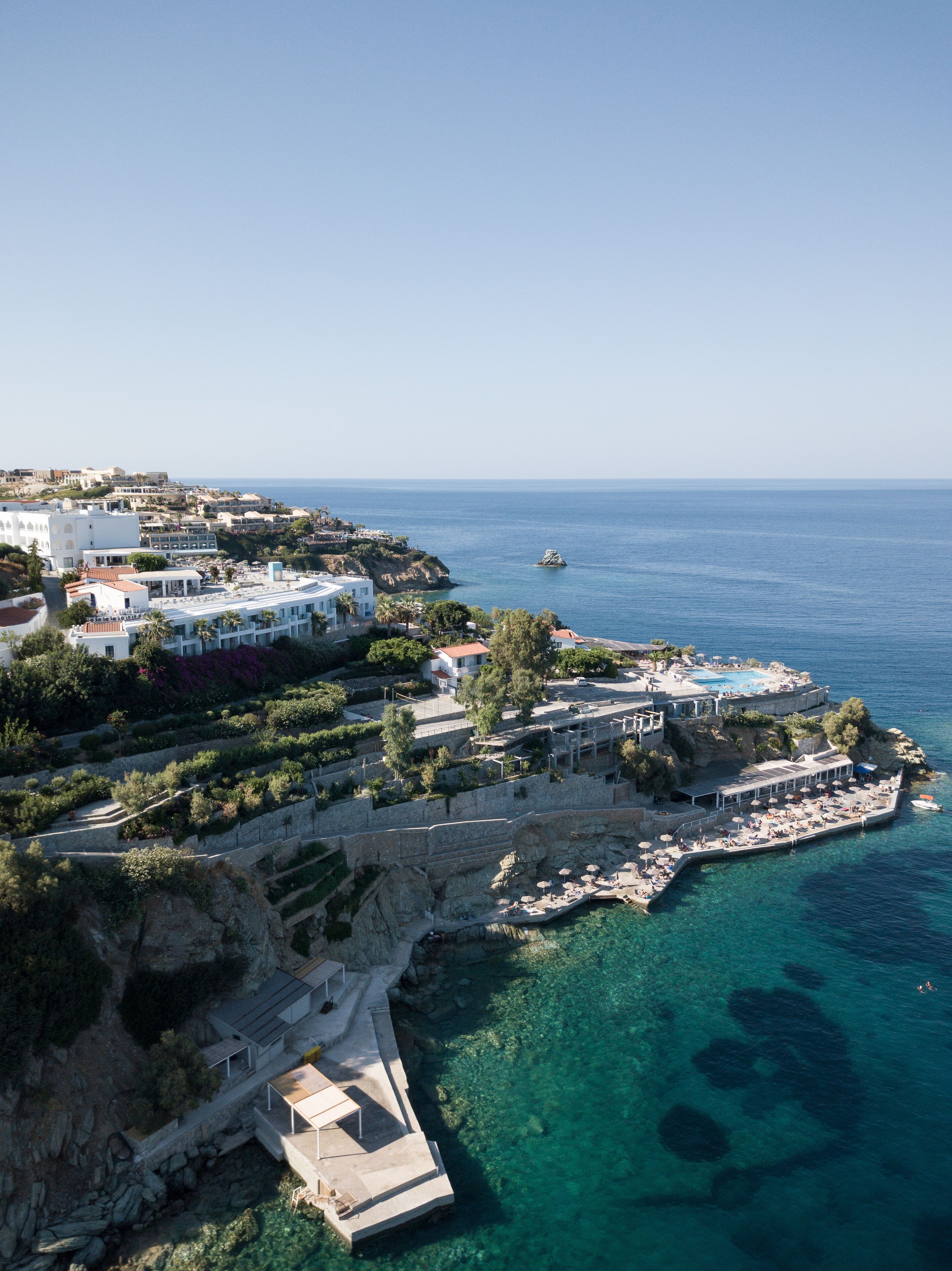 Un resort costero con zona de piscina, muelle y aguas azul turquesa.